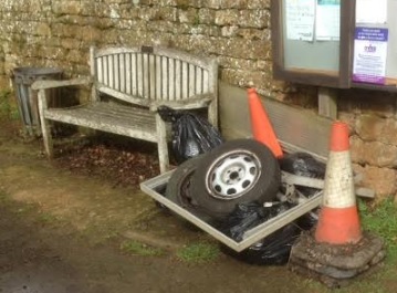 A pile of old tyres, traffics cones and bin bags, next to a wooden bench